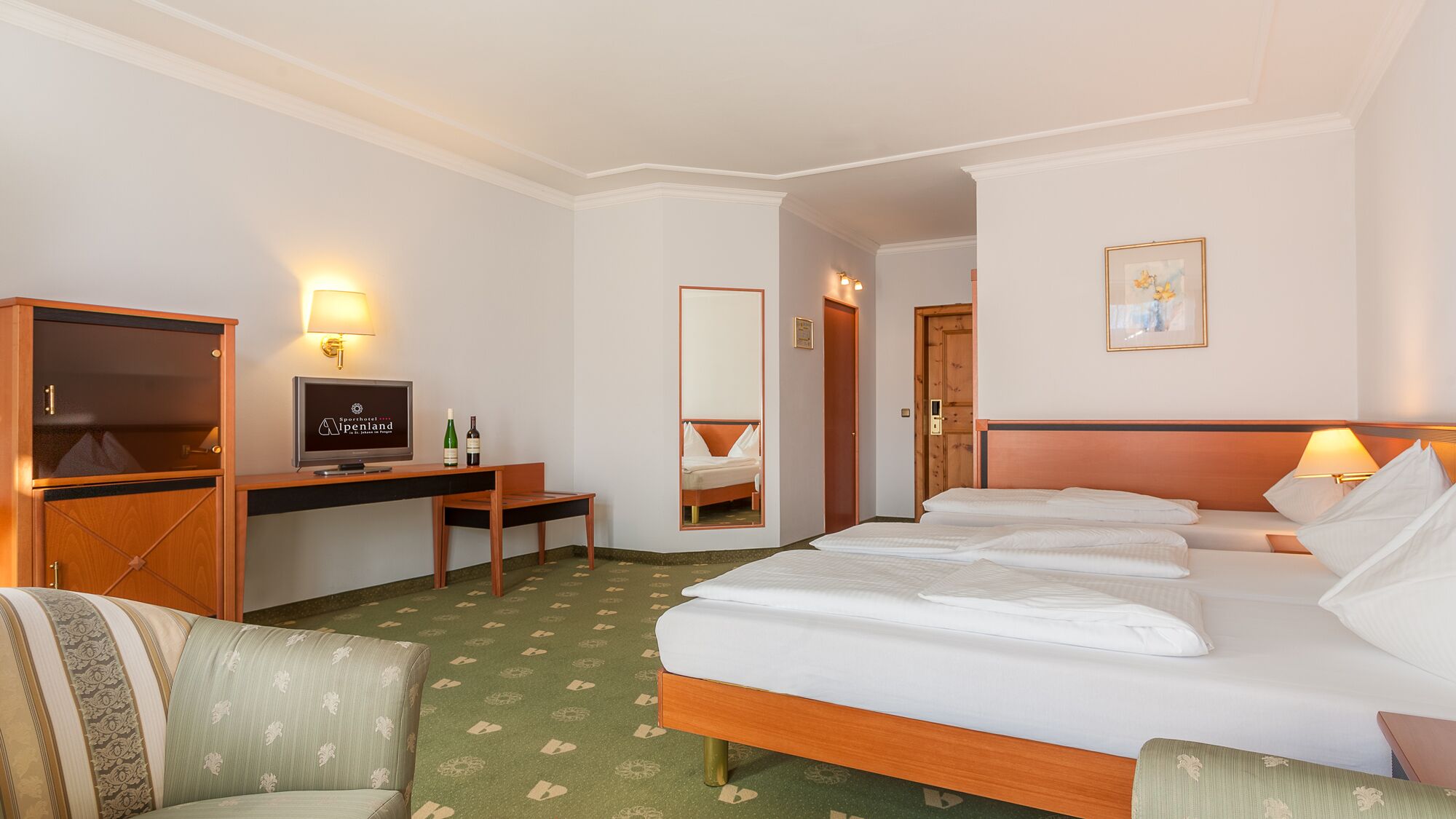 A hotel room with a bed, a desk with a television, a chair, and a mirror.
