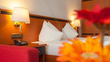 A hotel room with a bed, two bedside lamps, a telephone, and a red chair.