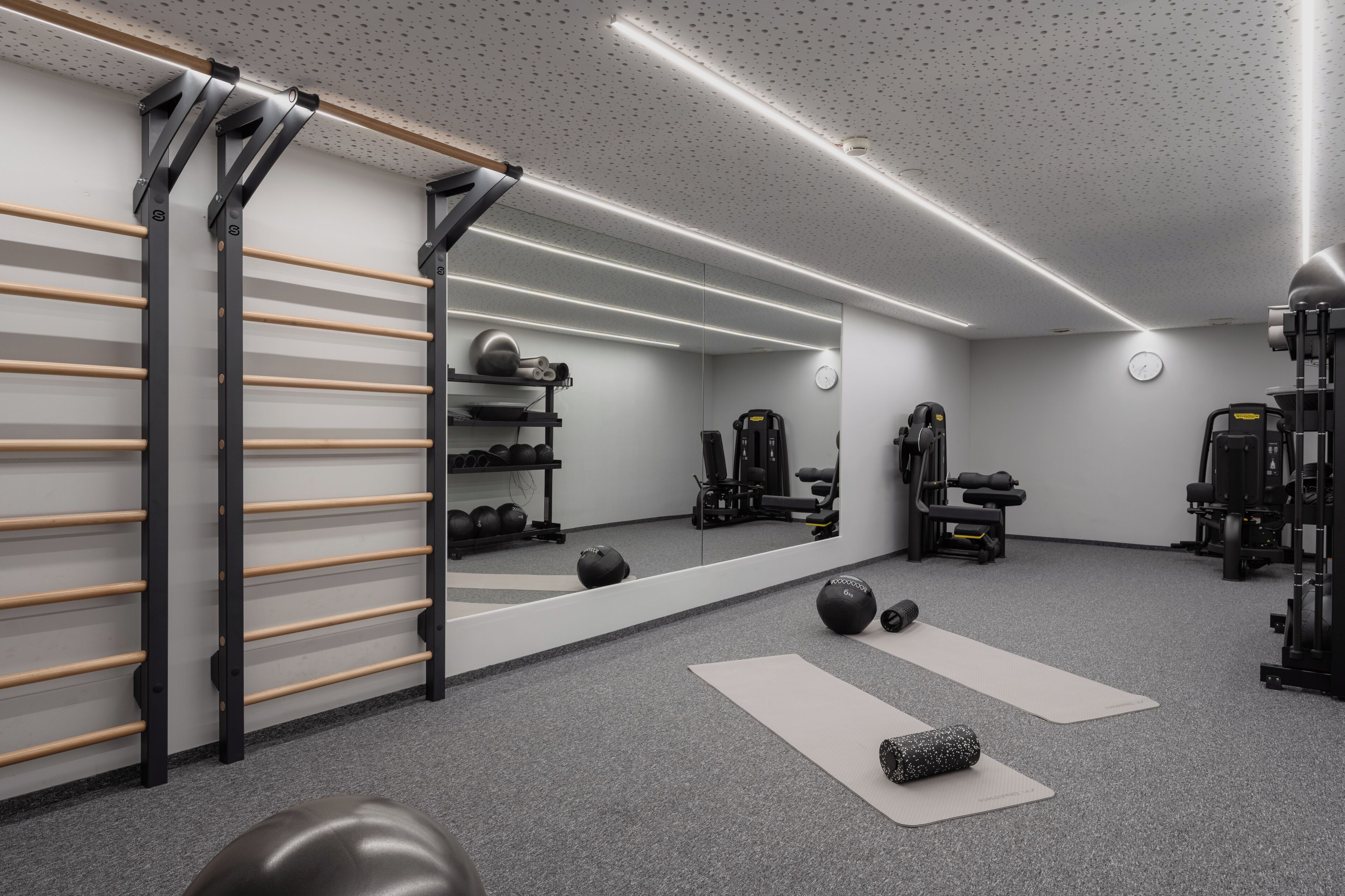 Une salle de sport équipée de matériel d’exercice, d’un miroir et d’un porte-serviettes en bois.