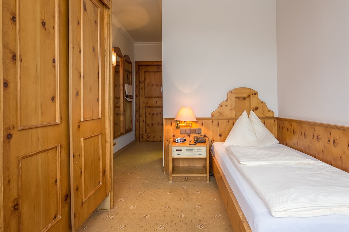 Quarto de hotel com cama de madeira, mesa de cabeceira com luminária e guarda-roupa de madeira.