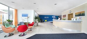 A modern reception area with a blue wall, a reception desk, and colorful chairs. - Hotel Michael (Prague)
