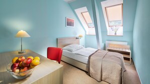 A bedroom with a bed, a desk with a lamp, a chair, a window, and a skylight.
