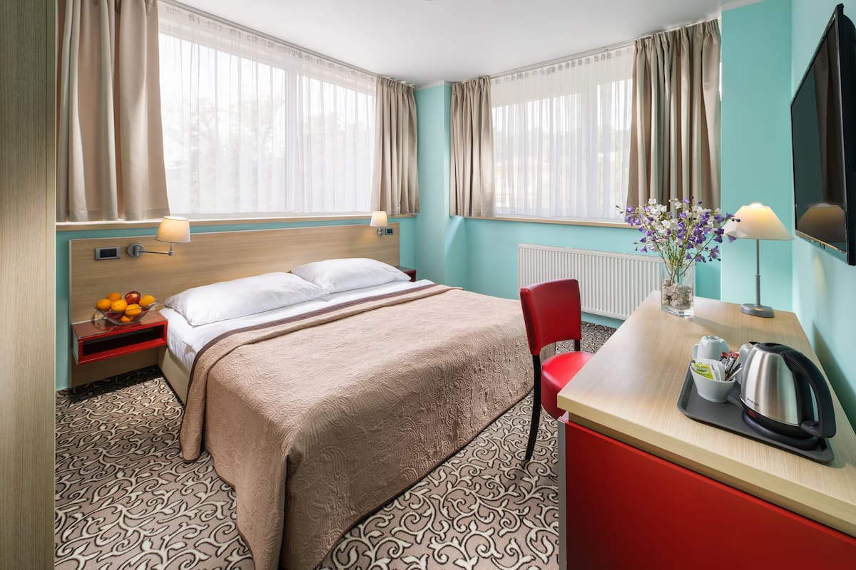 Hotellihuone, jossa on sänky, työpöytä, tuoli, televisio ja ikkuna, jossa on verhot.