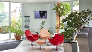 A modern interior with a glass door leading to a garden, a flat-screen TV on the wall, and a variety of potted plants.
