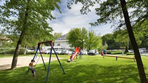 A park with a swing set, a red slide, and a seesaw.