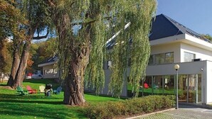 A modern two-story house with a flat roof, large windows, and a well-maintained lawn with outdoor seating.