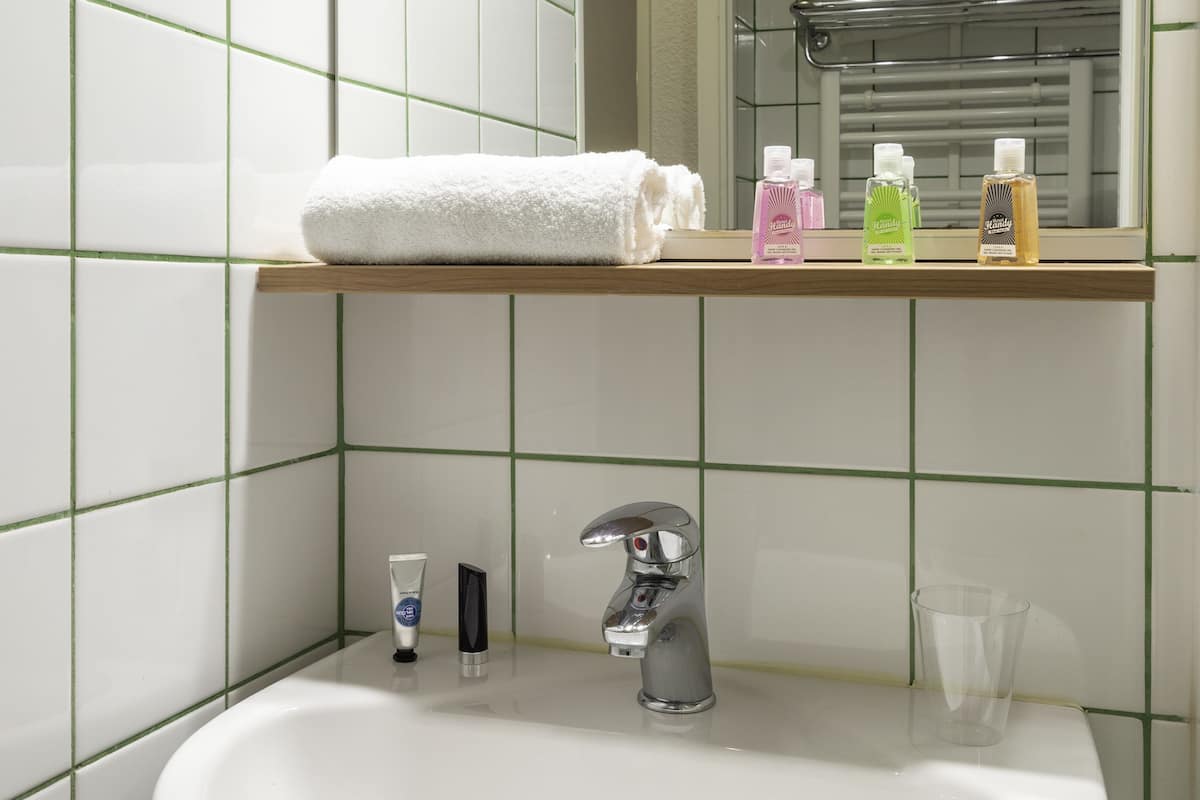 A bathroom with a white sink, a mirror, and a shelf with toiletries.