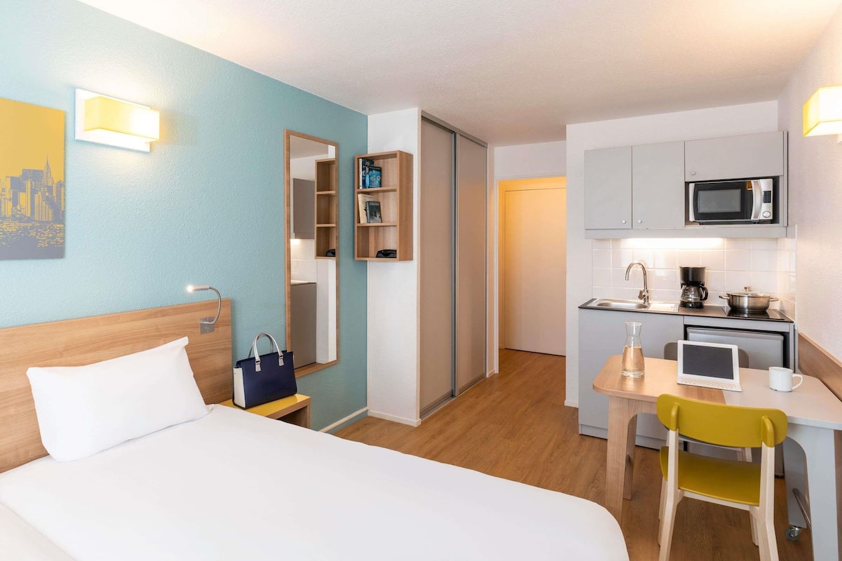 A hotel room with a bed, a desk with a chair, a microwave, a coffee maker, and a small kitchenette.