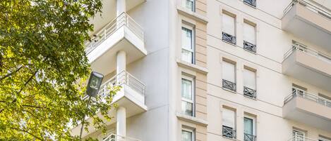A modern apartment building with balconies, large windows, and a sign for 'Adagio Apartment Hotel'.