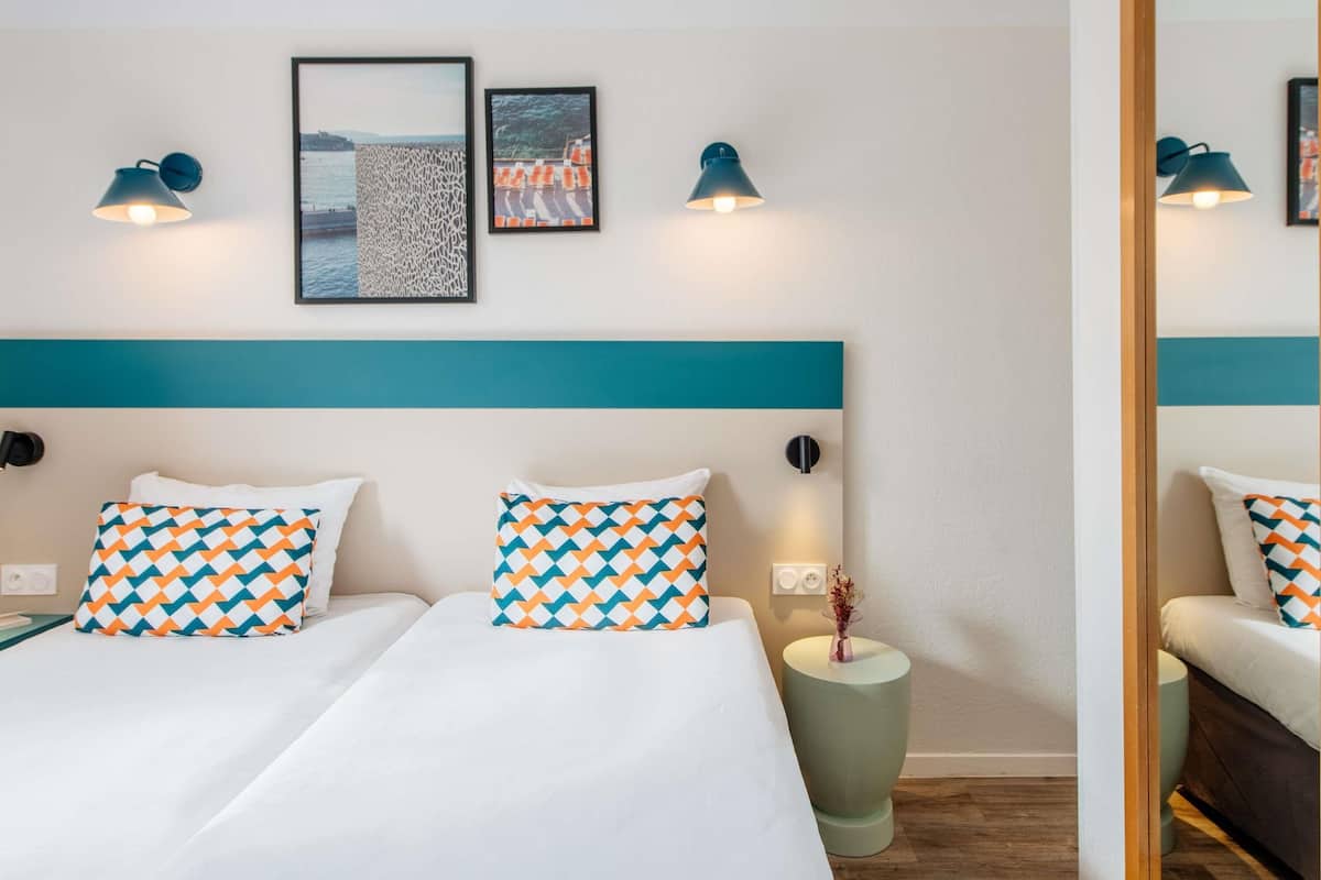 Une chambre d’hôtel avec un lit, deux oreillers, une table de chevet, un vase et des lampes fixées au mur.