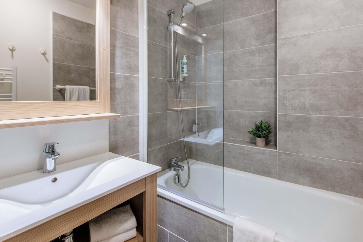 Une salle de bain moderne avec un lavabo blanc, une douche en verre et une petite plante en pot.
