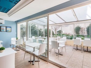 Un espace de restauration intérieur moderne, avec des tables et des chaises blanches, de grandes fenêtres et un mur bleu.