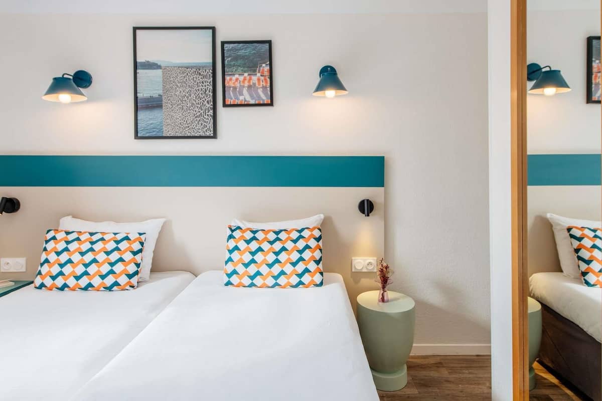 Une chambre d’hôtel avec un lit, deux lampes fixées au mur et deux tableaux encadrés.