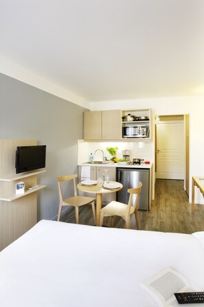 A compact hotel room with a kitchenette, a dining area, a TV, and a bed. - Aparthotel Adagio Access Marseille Prado Perier (Marseille)