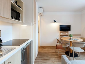 A modern kitchen with a built-in oven, a dining area with a round table and chairs, and a flat-screen TV mounted on the wall. - Aparthotel Adagio Access Marseille Prado Perier (Marseille)