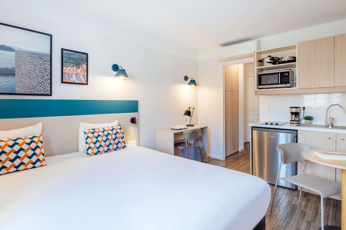 Une chambre d’hôtel équipée d’un lit, d’un bureau, d’une chaise, d’une petite table, d’un four à micro-ondes, d’une machine à café et d’un lave-vaisselle.