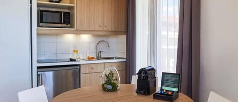 A compact kitchen with a microwave, kettle, and sink. There's a dining table with chairs, a small plant, and a charging station.