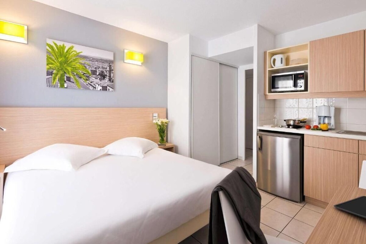 A hotel room with a bed, a small kitchenette, and a bathroom.