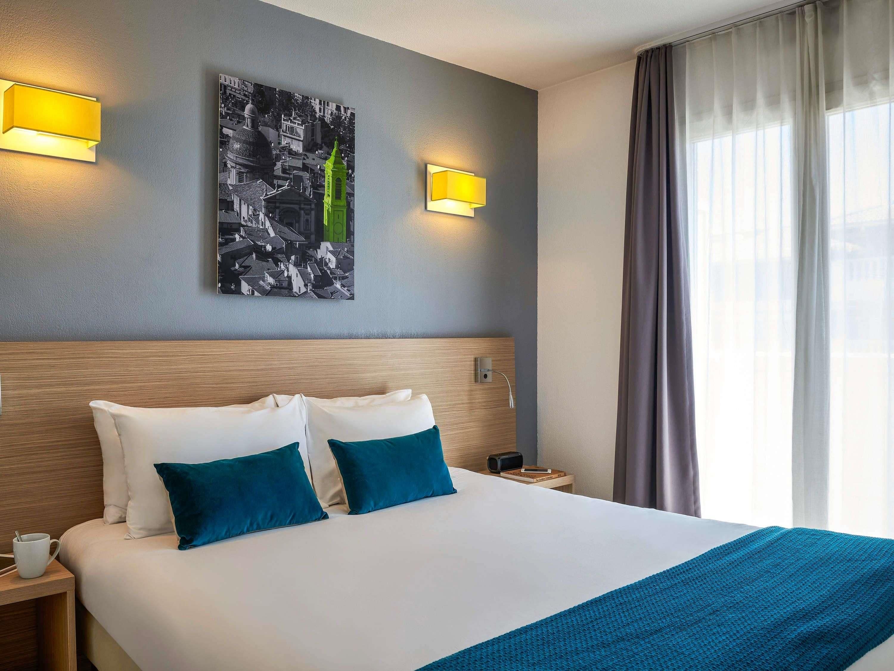 Et hotelværelse med en stor seng, to puder, et natbord med en kop og et billede på væggen.