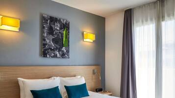 A hotel room with a large bed, two pillows, a bedside table with a cup, and a painting on the wall.
