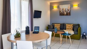 Un salon moderne avec une table à manger ronde, un canapé vert et un téléviseur à écran plat fixé au mur.