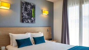 A hotel room with a large bed, two pillows, a nightstand, a lamp, and a painting on the wall. - Aparthotel Adagio Access Nice Magnan (Nice)