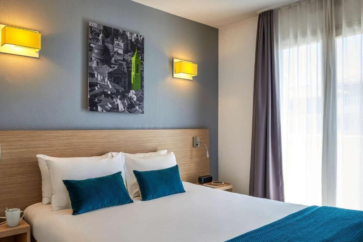 A hotel room with a large bed, two pillows, a nightstand, a lamp, and a painting on the wall.