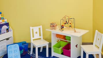 Ein Spielbereich für Kinder mit zwei weißen Stühlen, einem kleinen Tisch mit Spielzeug und Aufbewahrungsboxen.