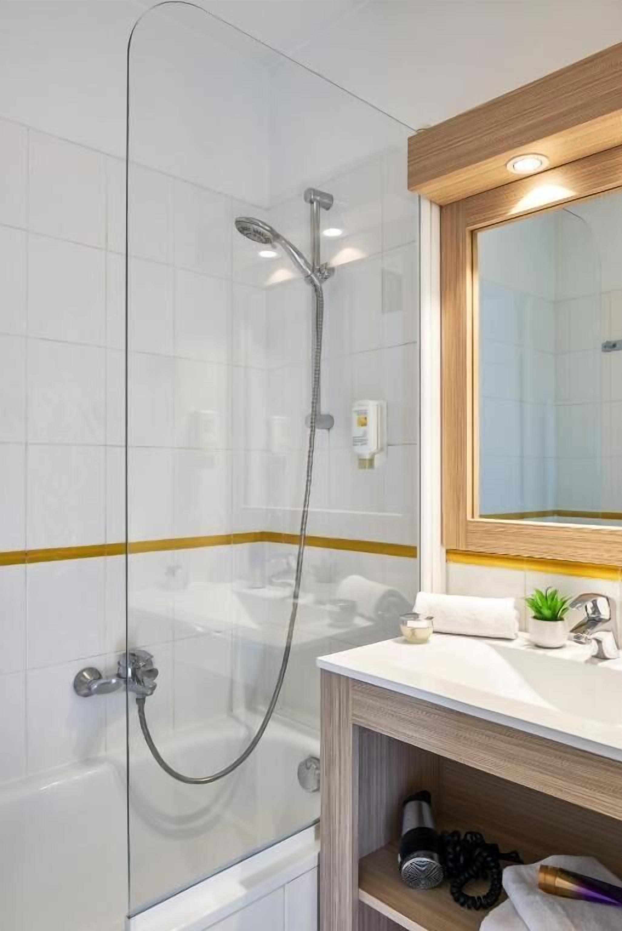 Un baño moderno con ducha de vidrio, tocador de madera con espejo y pared de azulejos blancos.