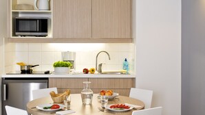 Une cuisine moderne avec un coin repas, comprenant un lave-vaisselle en acier inoxydable, un four à micro-ondes et un évier avec un robinet. Une table est dressée avec des assiettes, des verres et un vase de fleurs.