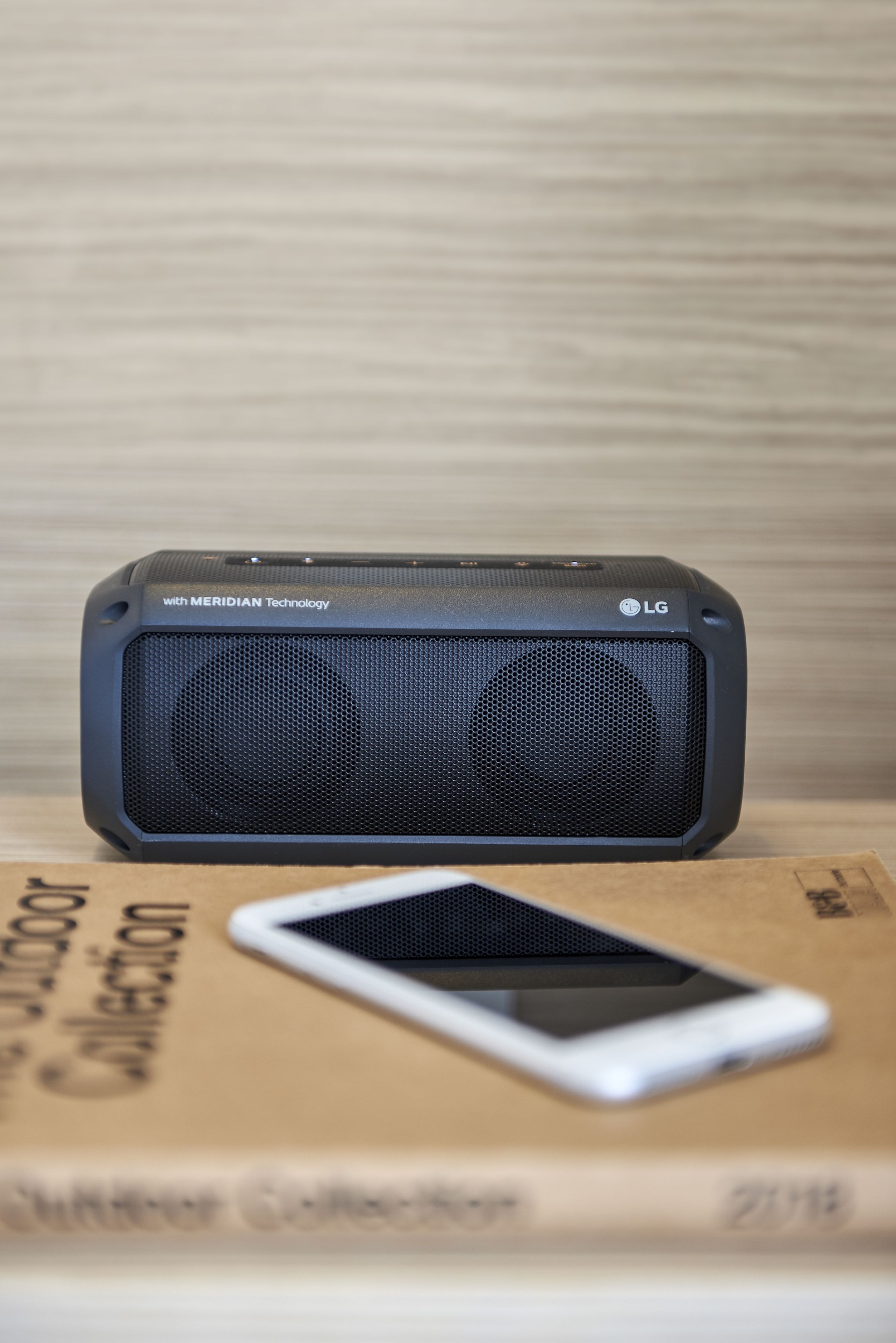 A black LG speaker with Meridian Technology on a wooden surface.