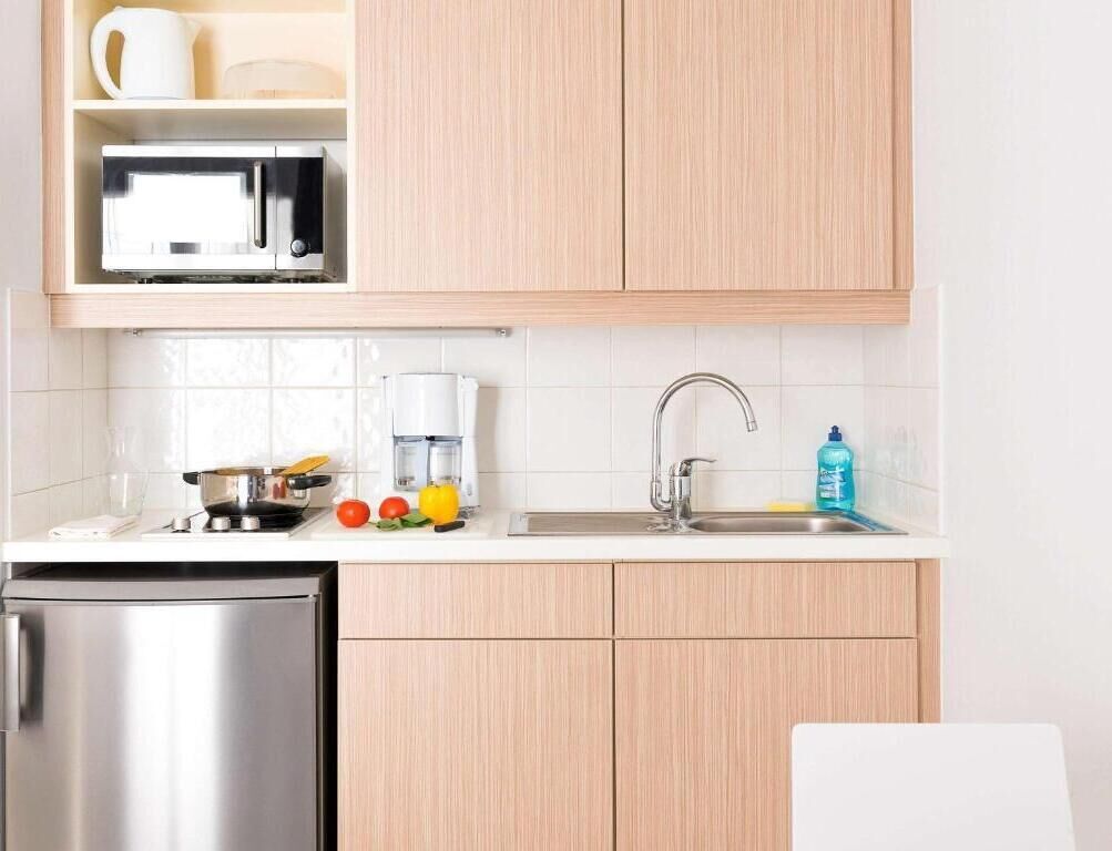 Une cuisine avec des meubles de couleur bois clair, un réfrigérateur en acier inoxydable, un four à micro-ondes, une machine à café et un évier avec un robinet.