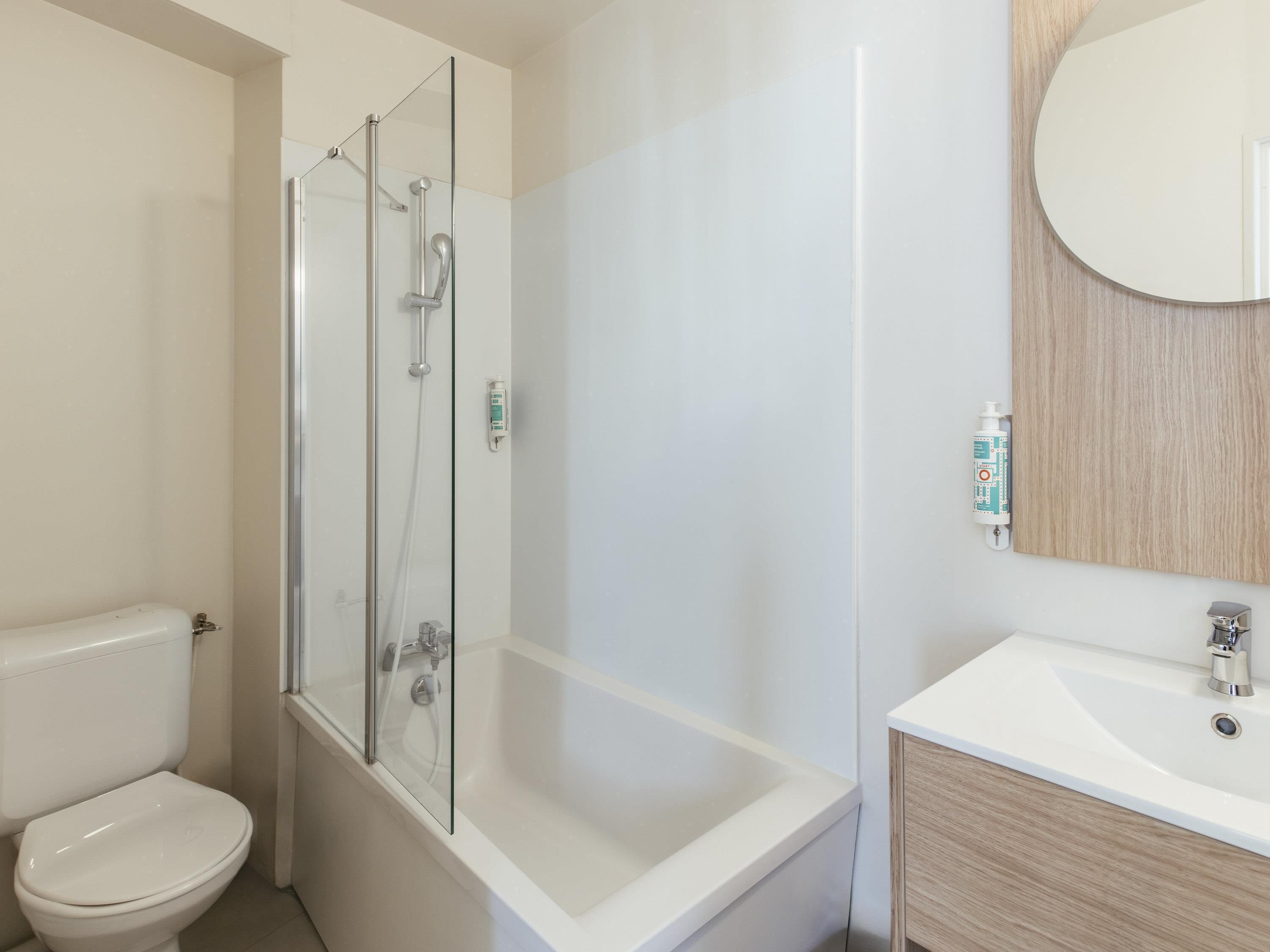 A bathroom with a glass-enclosed shower, a toilet, and a sink with a mirror.