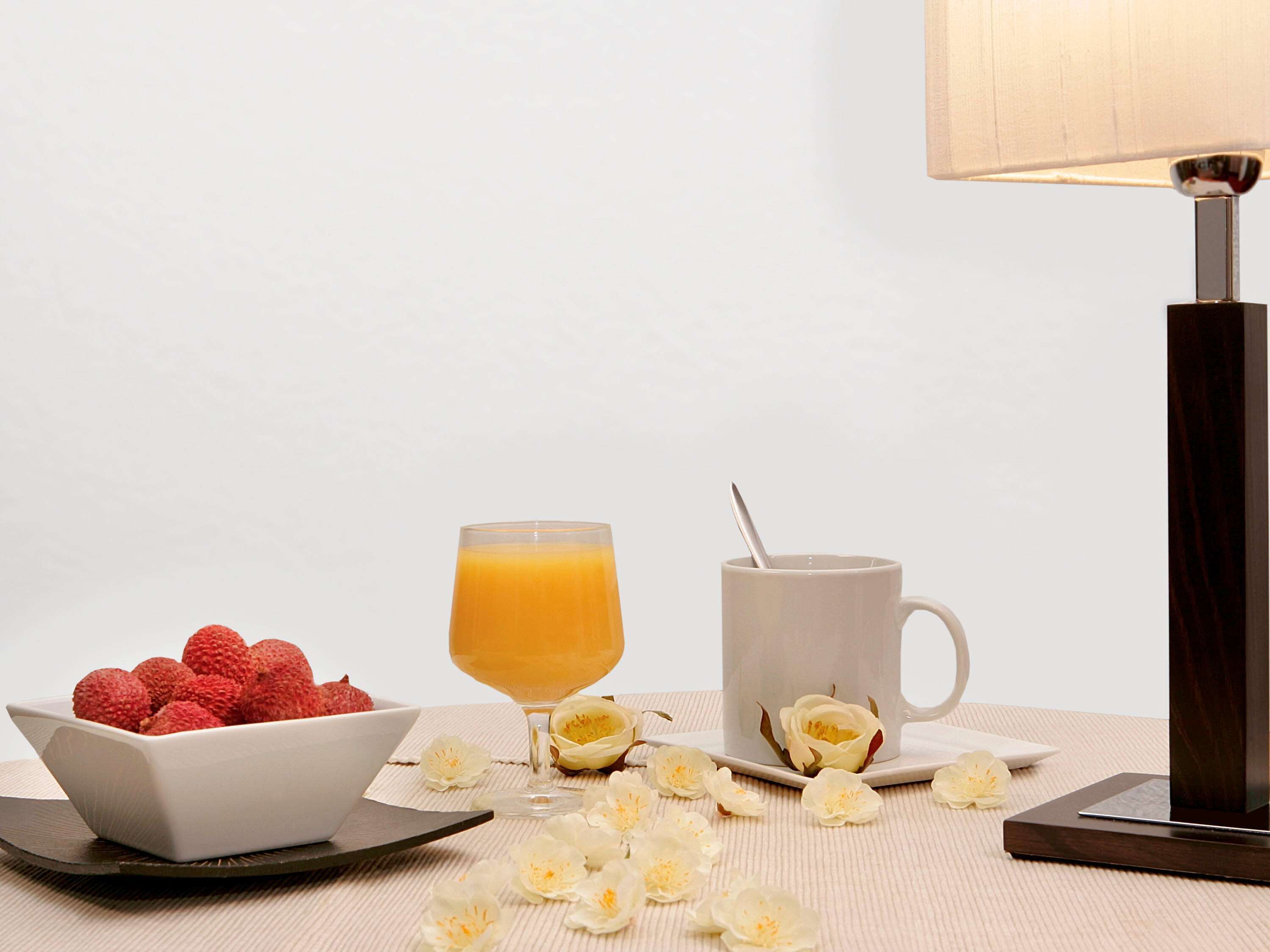 Uma mesa com uma tigela de morangos, um copo de suco de laranja, uma caneca com uma colher e flores brancas espalhadas.