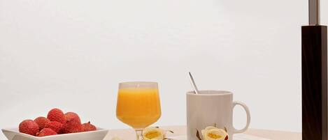 Uma mesa com uma tigela de morangos, um copo de suco de laranja, uma caneca com uma colher e flores brancas espalhadas.