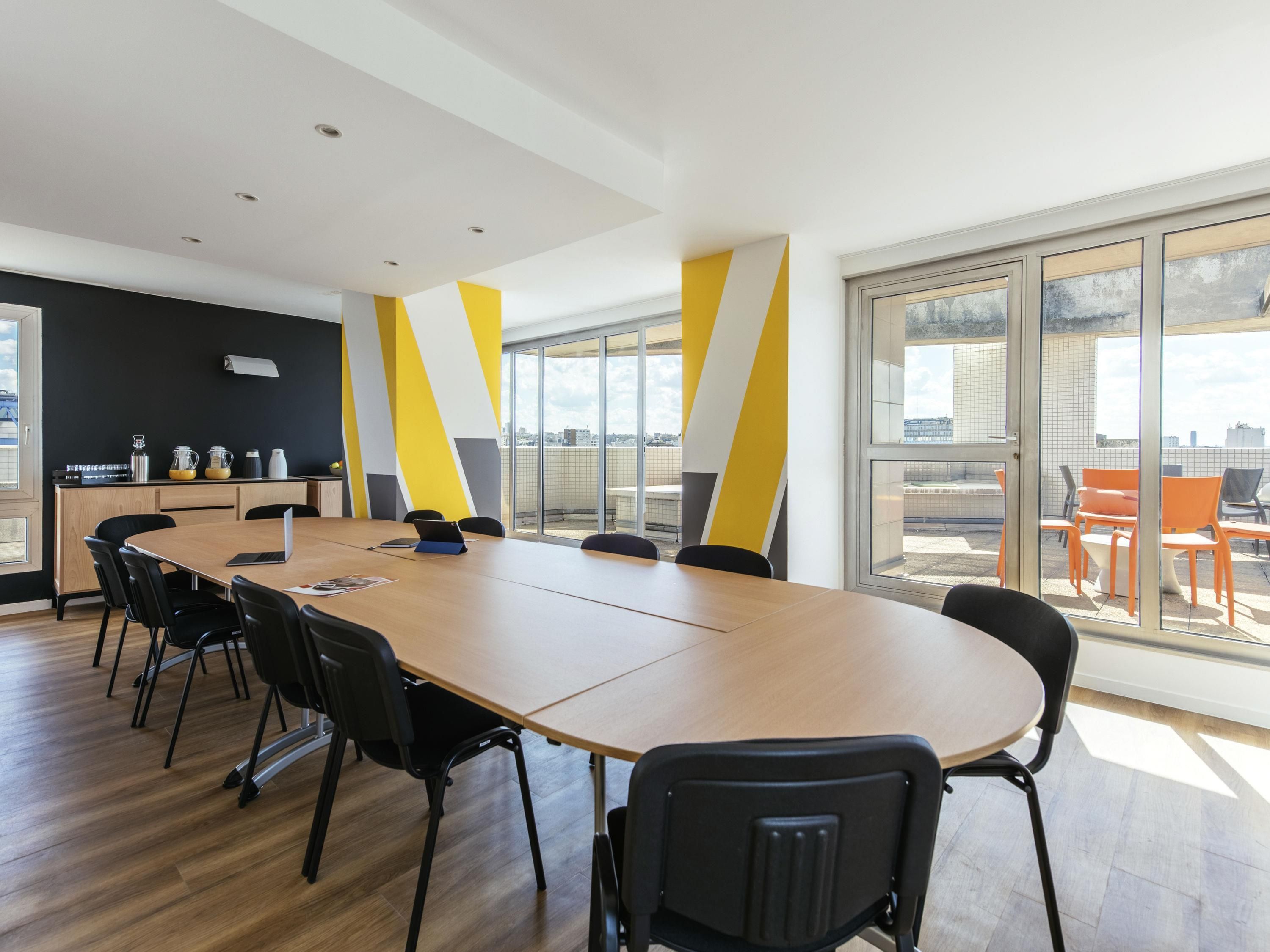 A conference room with a long table, black chairs, a coffee station, and large windows with a city view.