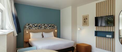 A hotel room with a bed, a round table, a TV mounted on the wall, and a window with curtains.