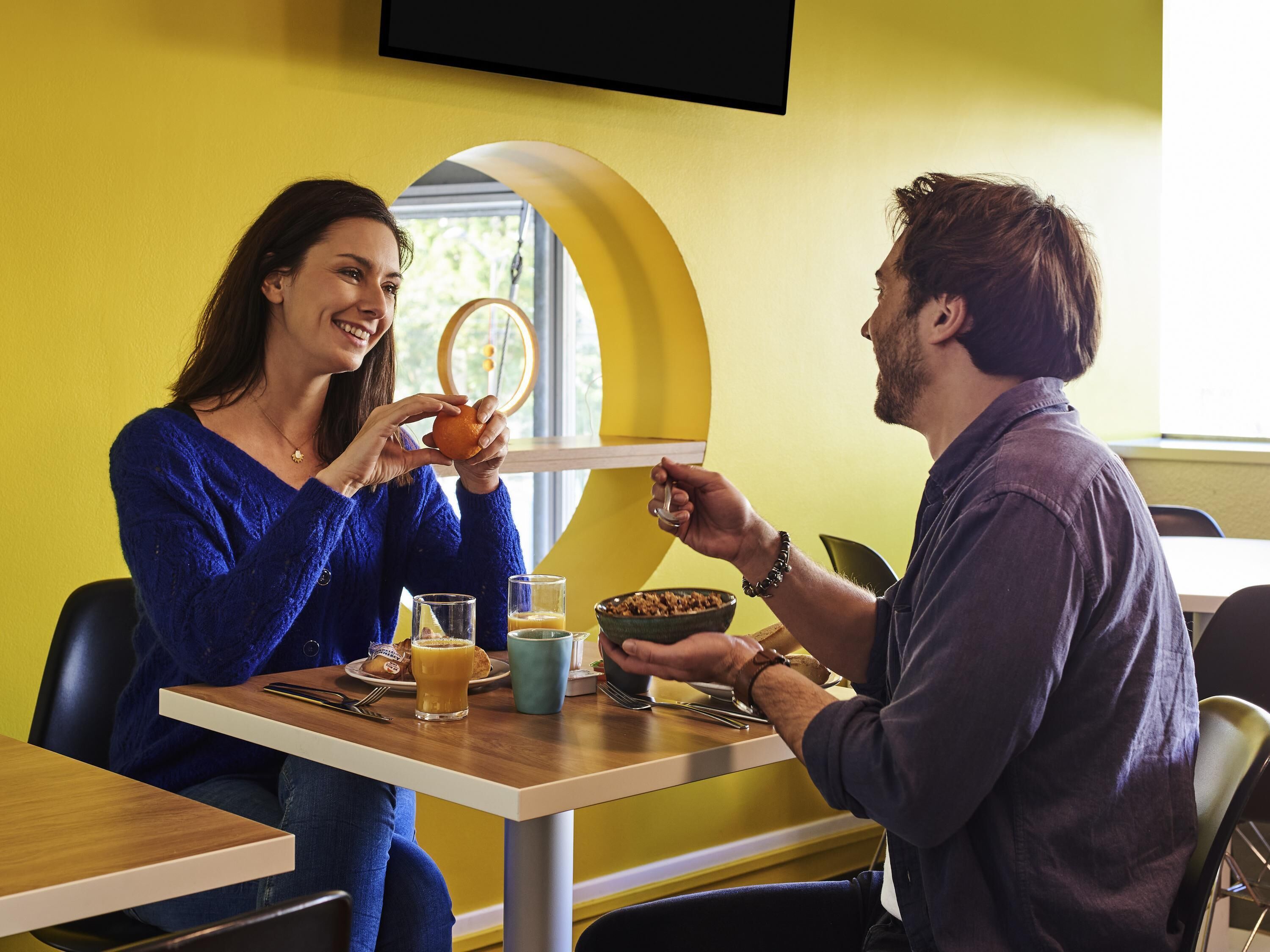A dining area with a table set for two, a bowl of cereal, a glass of orange juice, and a plate with a muffin.
