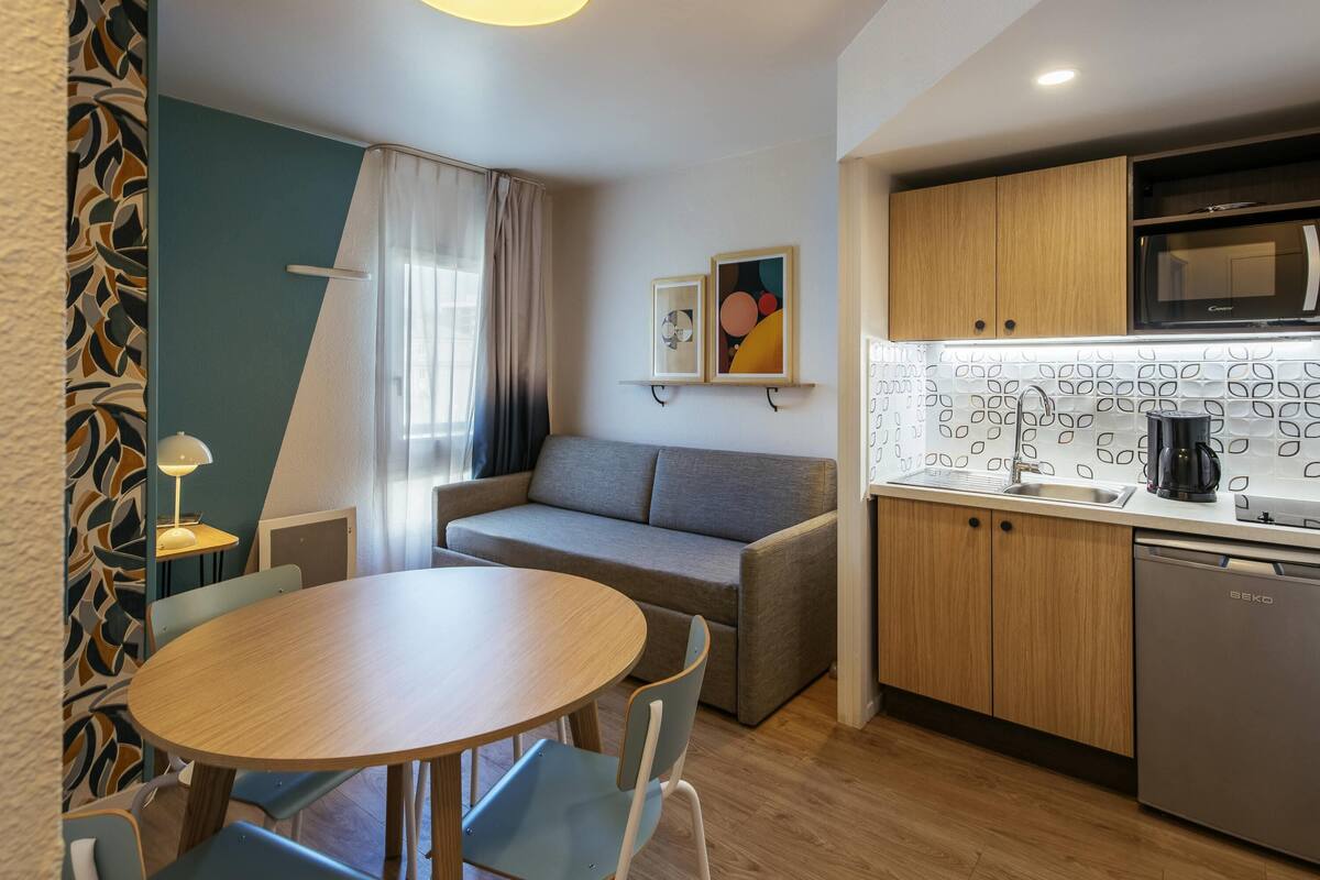 Ein kompakter Wohnbereich mit Sofa, Esstisch, Küchenzeile mit Mikrowelle und Kaffeemaschine.