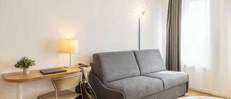 Una sala de estar moderna con un sofá, un escritorio con una lámpara, una silla, un teléfono inteligente y una taza de café.