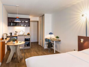 A compact hotel room with a bed, a desk, a chair, a small table, a kitchenette, and a bathroom. - Aparthotel Adagio Access Toulouse Jolimont (Toulouse)
