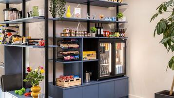 A kitchenette with shelves stocked with food items, a refrigerator, and a small plant.