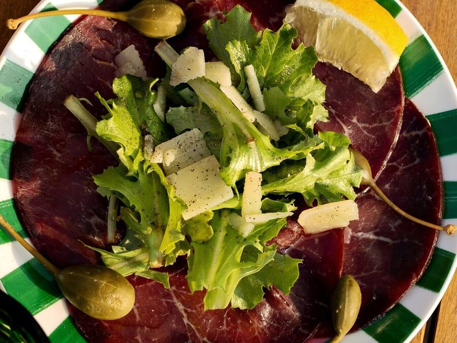Ein Teller Essen mit einem grün-weißen, gestreiften Rand, der rotes Fleisch, grüne Blattsalate und ein Zitronenzwischenstückchen enthält.