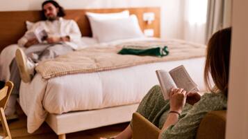 Een slaapkamer met een bed, een persoon die een boek leest, en een andere persoon die in bed ligt.