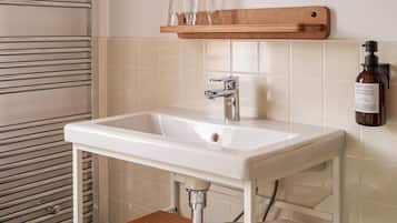 A bathroom with a white sink, chrome faucet, and a wooden shelf above it.