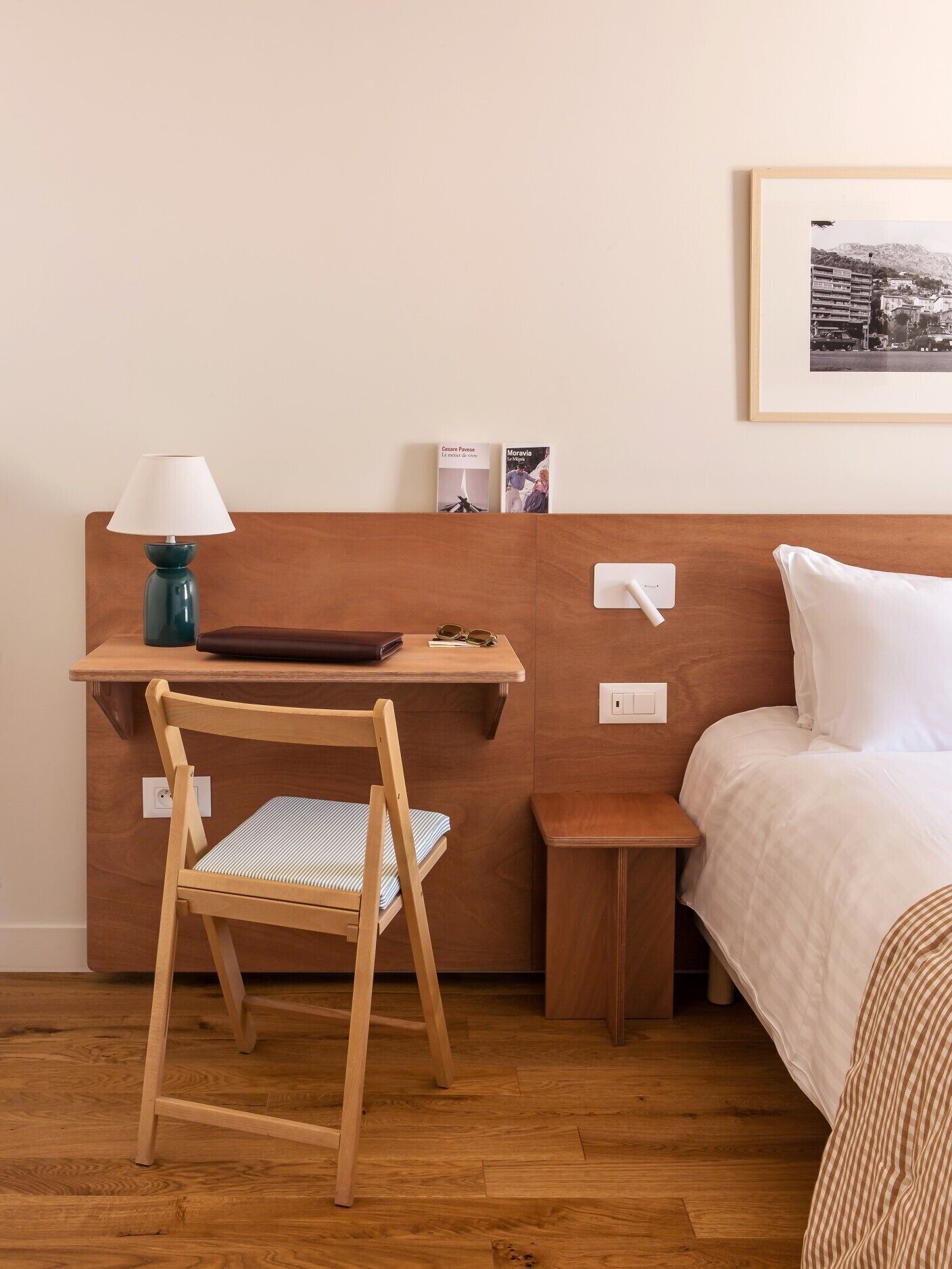 Un dormitorio ordenado con un escritorio de madera, una silla, una mesita de noche y una cama.
