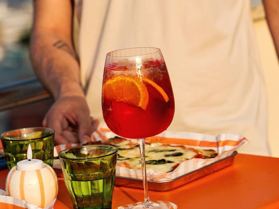 A table with a glass of red drink, a green glass, a striped teapot, and a tray with food.