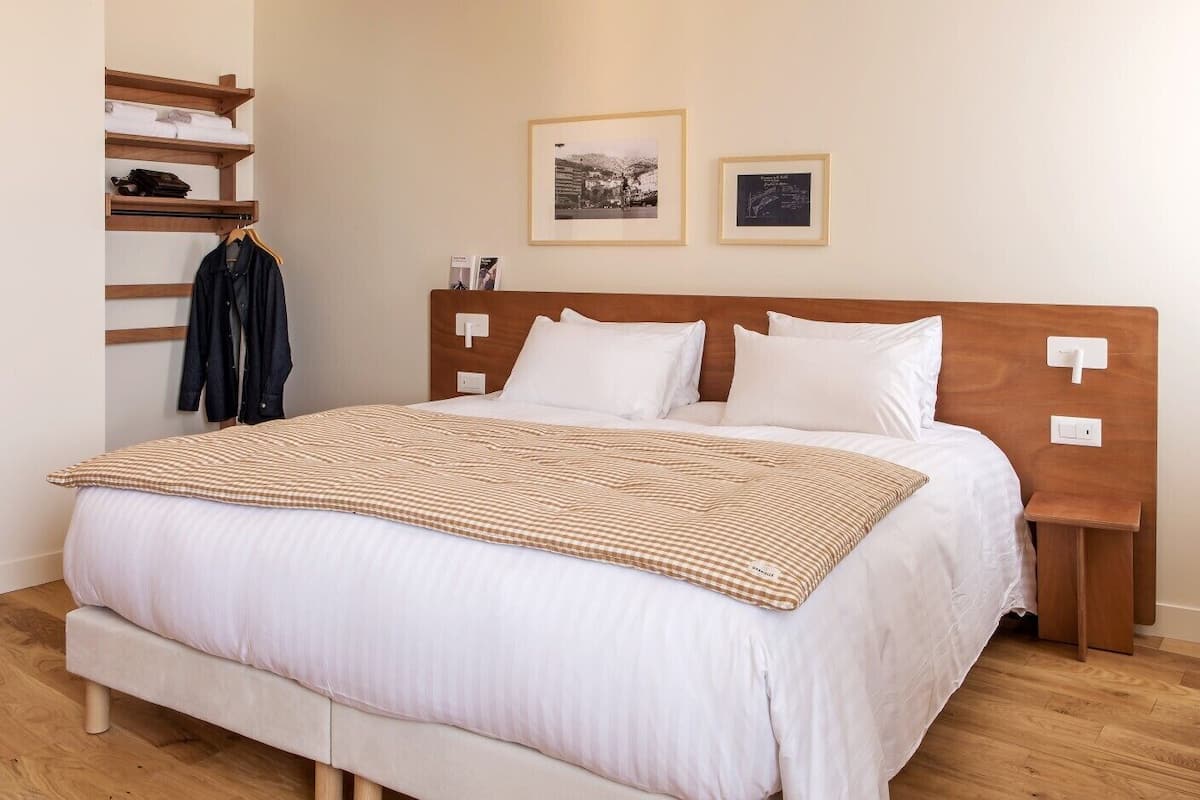Una cama bien hecha con una colcha a cuadros, un cabecero de madera y dos mesitas de noche.
