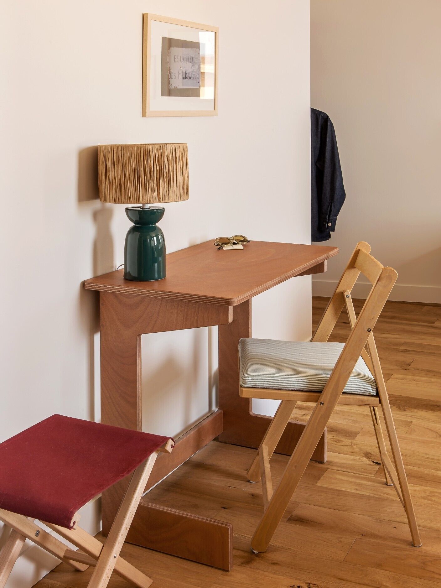 A small wooden table with a lamp, a pair of glasses, and a framed picture on the wall.