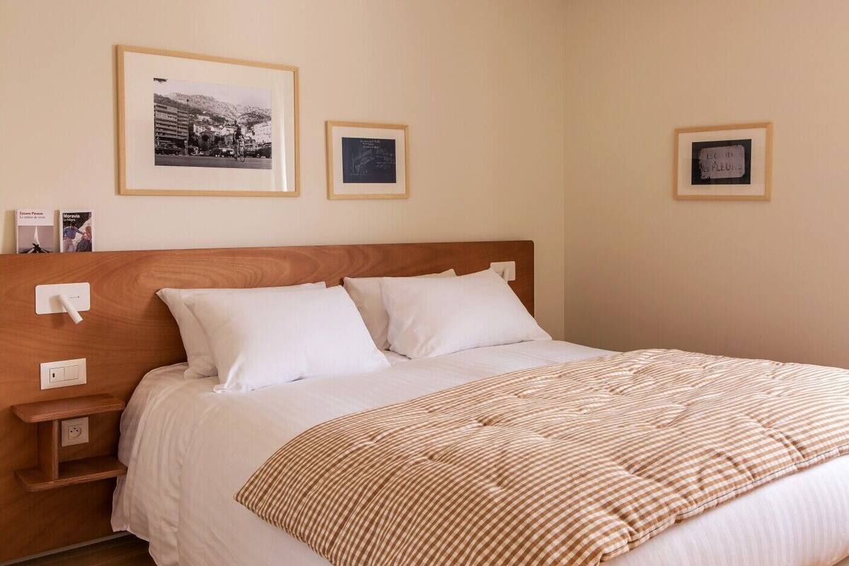 Una cama bien hecha con ropa de cama blanca y una manta a rayas, un cabecero de madera y dos cuadros en la pared.